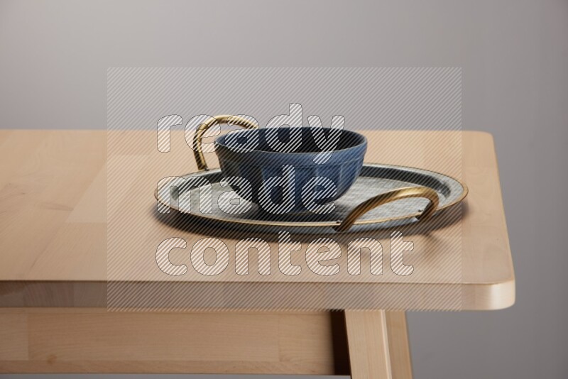 blue bowl placed on a rounded stainless steel metal tray with golden handels on the edge of wooden table