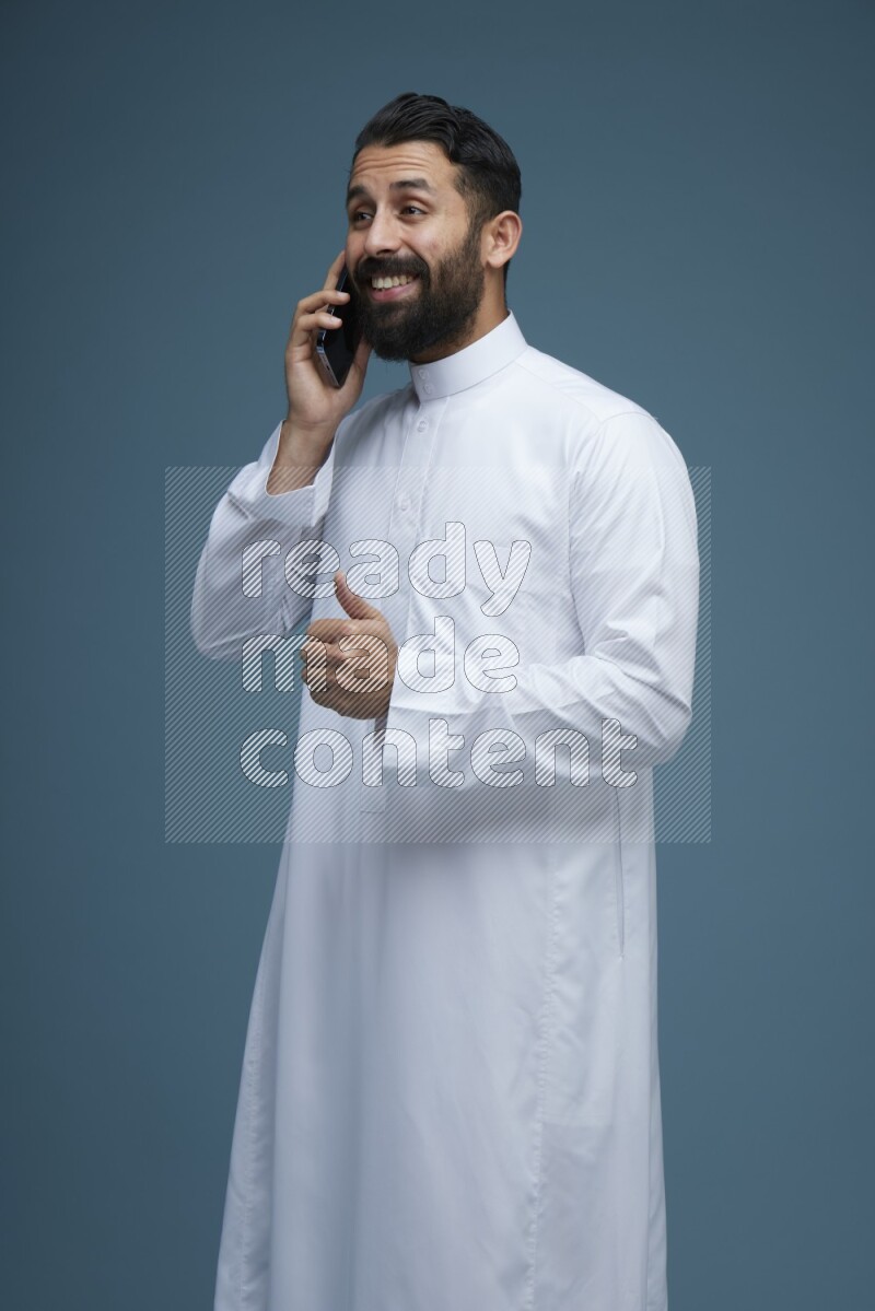 A man having a call on a blue background wearing Saudi Thob