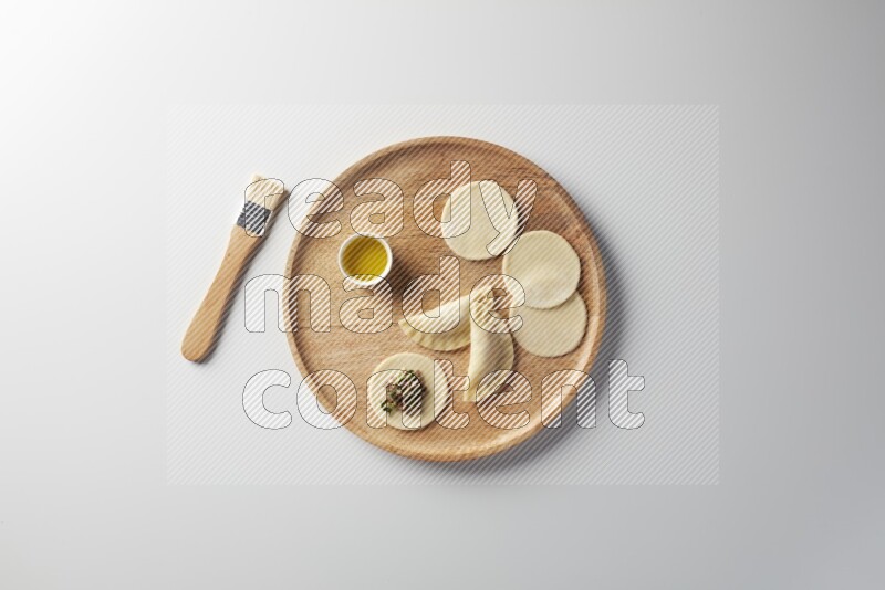 two closed sambosas and one open sambosa filled with meat while oil with oil brush aside in a wooden dish on a white background