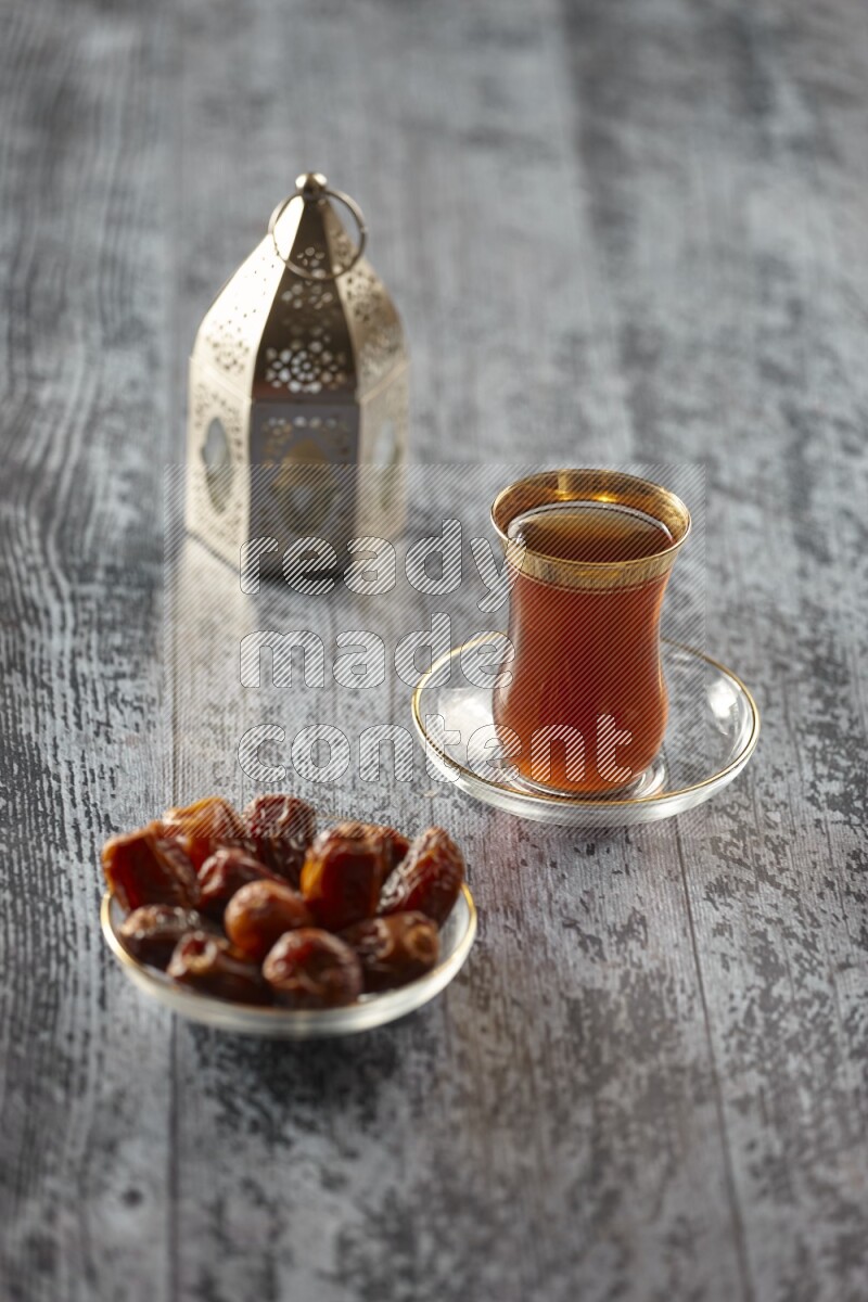 A silver lantern with different drinks, dates, nuts, prayer beads and quran on grey wooden background