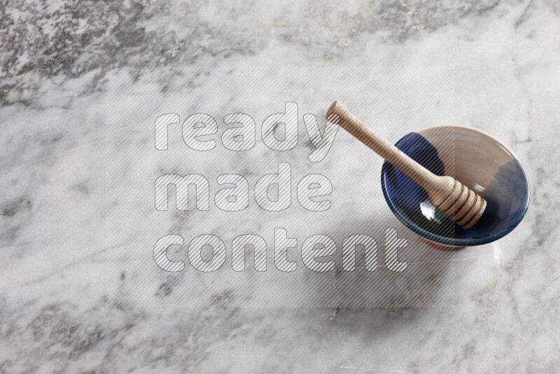 Multicolored pottery bowl with wooden honey dipper in it on grey marble background
