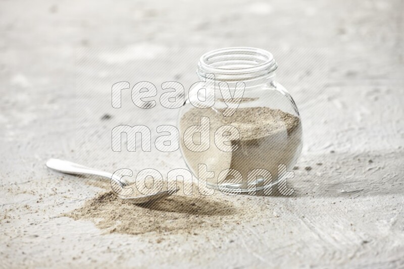 Herbal Glass jar full of white pepper powder and metal spoon full of powder on textured white flooring