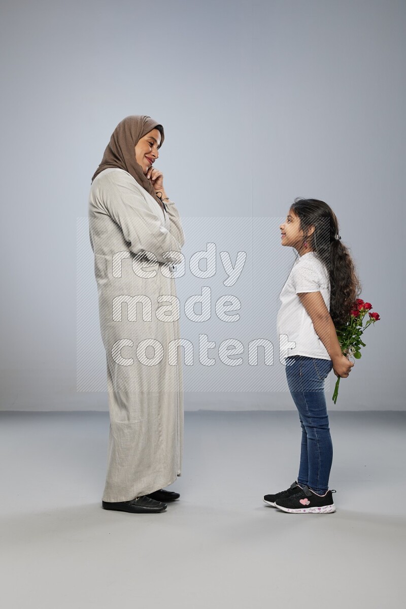 A girl standing giving flowers to her mother on gray background