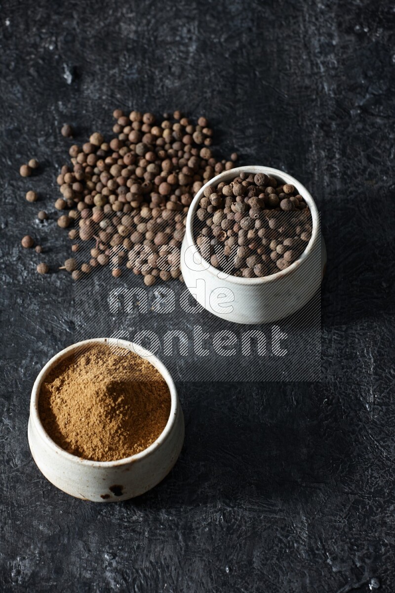 وعاءان بيج، أحدهما ممتلئ ببودرة بهار الفلفل الحلو والآخر بالحبوب وكلاهما متناثران على خلفية سوداء