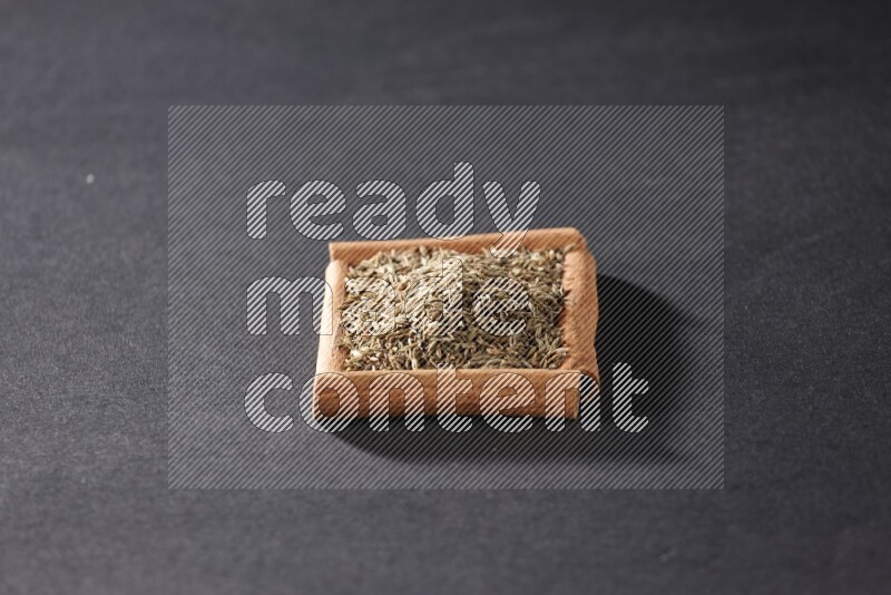 أربعة من أعواد القرفة مكونة شكل مربع بداخلها حبوب الكمون علي خلفية سوداء