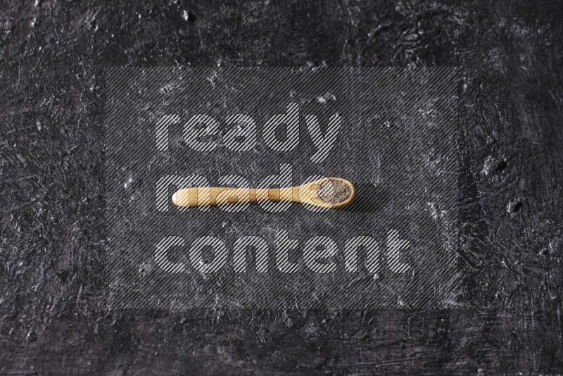 A wooden spoon full of black pepper powder on a textured black flooring