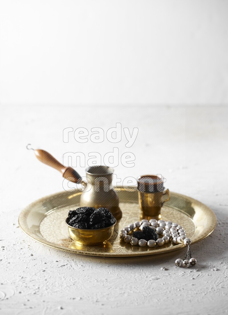 Dried plums in a metal bowl with coffee and prayer beads on a tray in a light setup