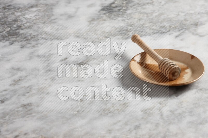 Multicolored pottery plate with wooden honey dipper in it on grey marble background
