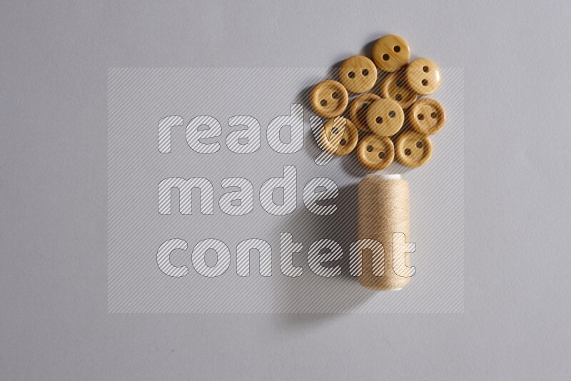 A beige sewing thread spool with colored buttons on grey background