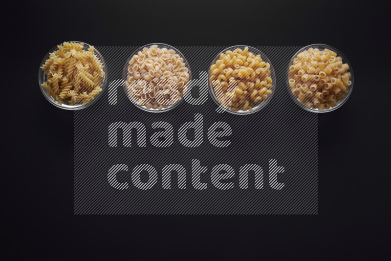 Different pasta types in glass bowls on black background