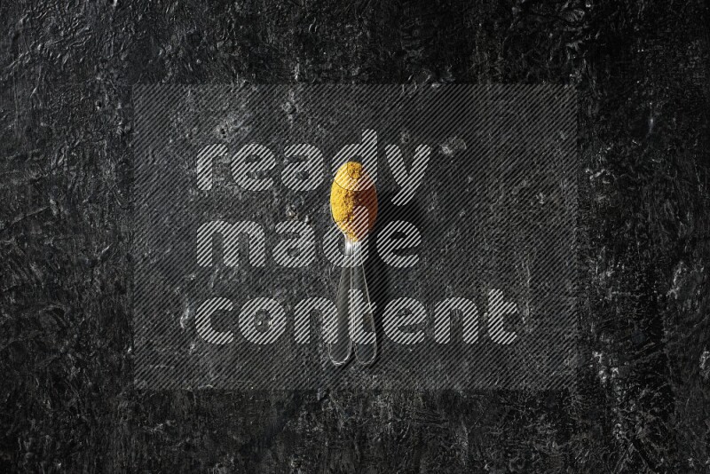 2 metal spoons full of turmeric powder on a textured black background