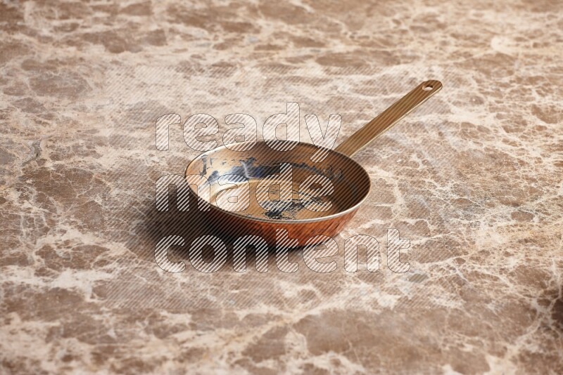 A small copper pan on beige marble background