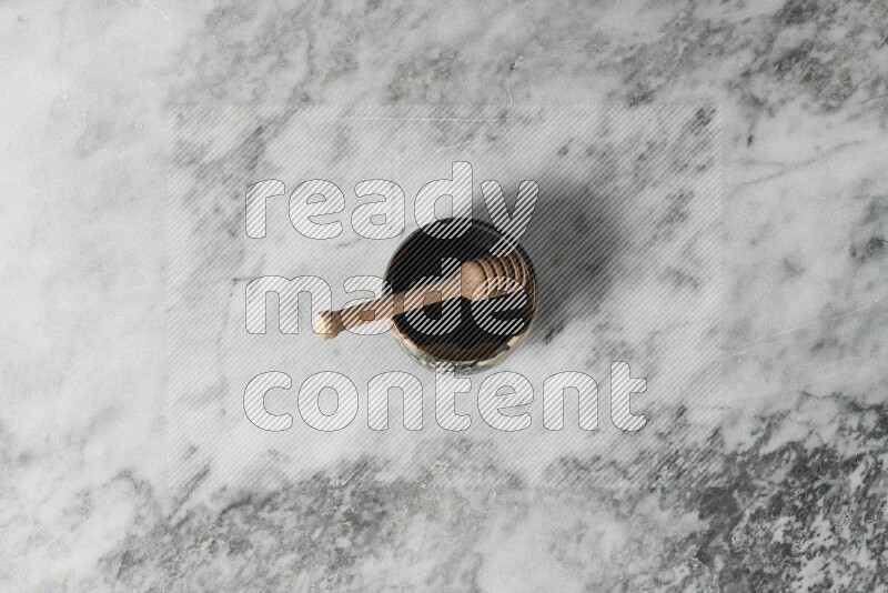 Multicolored pottery bowl with wooden honey dipper in it on grey marble background
