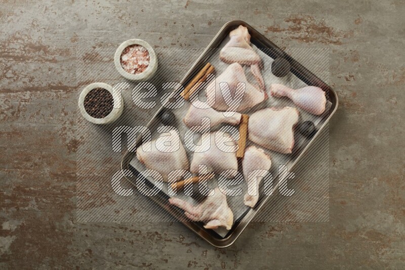 Mixed fresh chicken pieces in an oven tray on a textured rustic background
