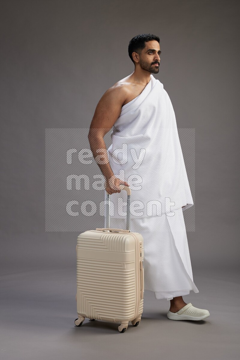 A man wearing Ehram Standing holding traveling bag on gray background