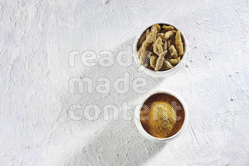 2 beige pottery bowl full of turmeric powder and dried turmeric whole fingers on textured white flooring