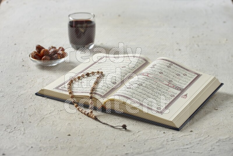 Quran with dates, prayer beads and different drinks all placed on textured white background