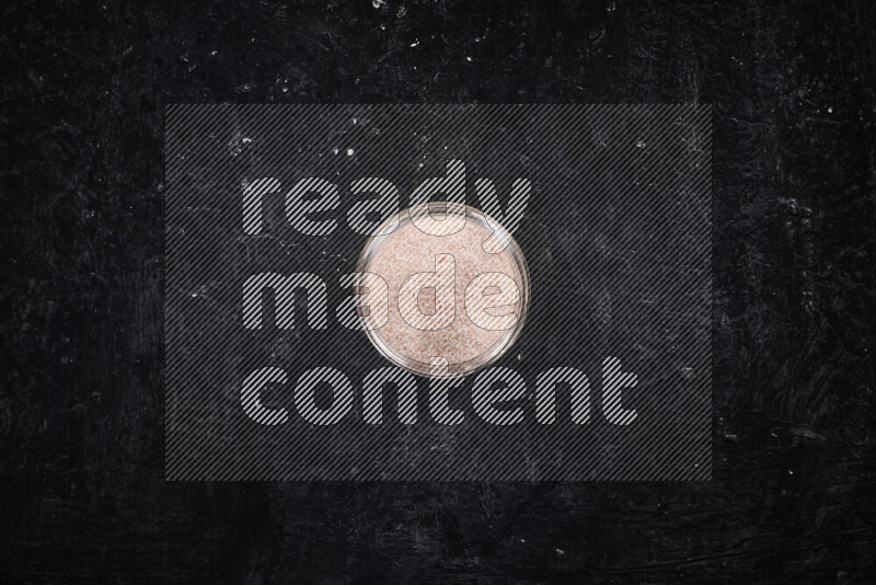 وعاء زجاجي ممتلئ بملح الهيمالايا الناعم على خلفية سوداء