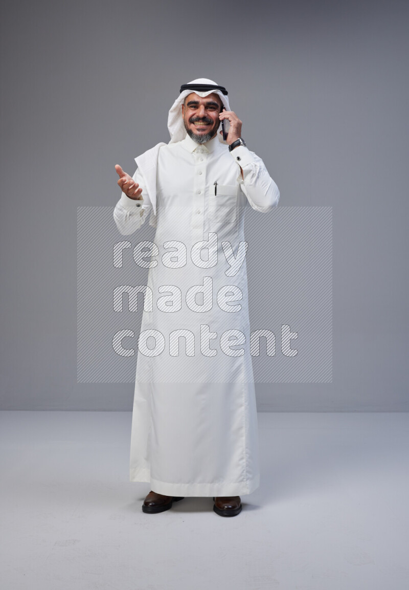 Saudi man Wearing Thob and white Shomag standing talking on phone on Gray background