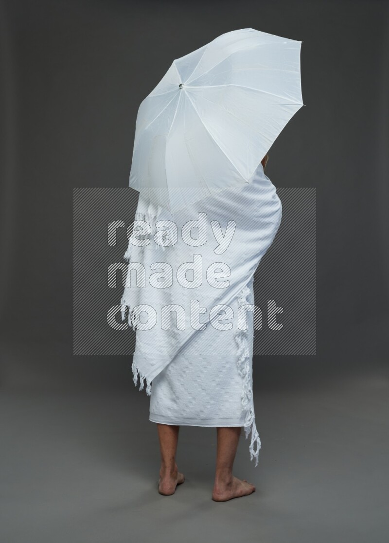 A man wearing Ehram Standing holding umbrella on gray background