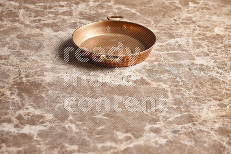 A small copper pan on beige marble background
