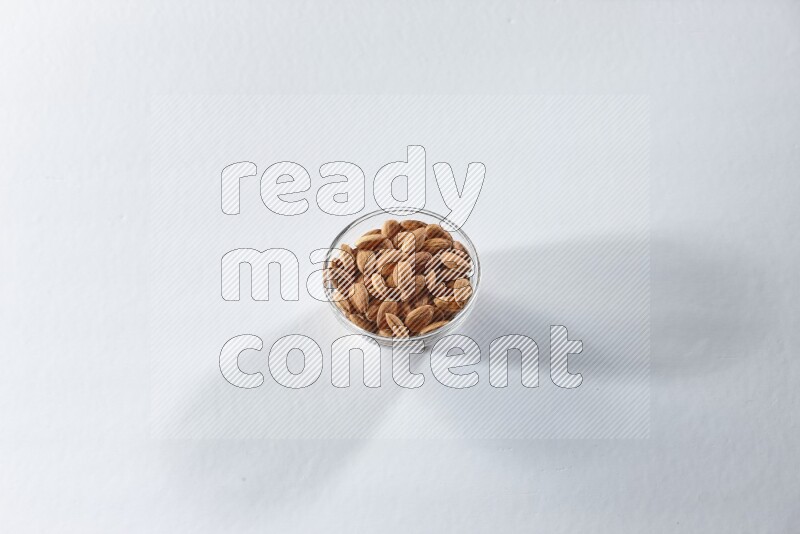 A glass bowl full of peeled almonds on a white background in different angles