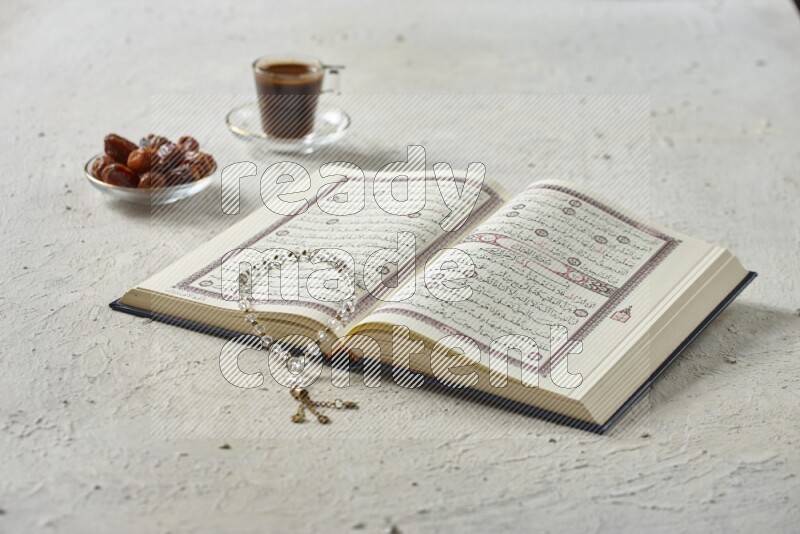 Quran with dates, prayer beads and different drinks all placed on textured white background