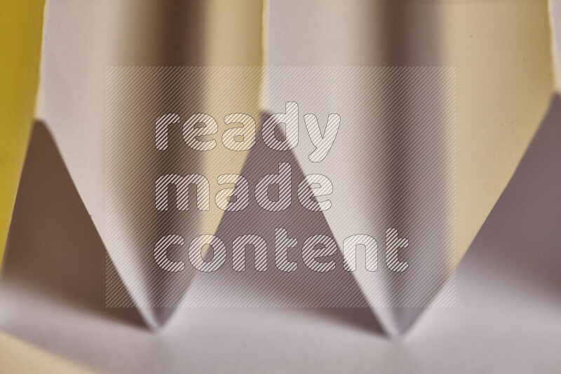 A close-up abstract image showing sharp geometric paper folds in white gradients and warm tones