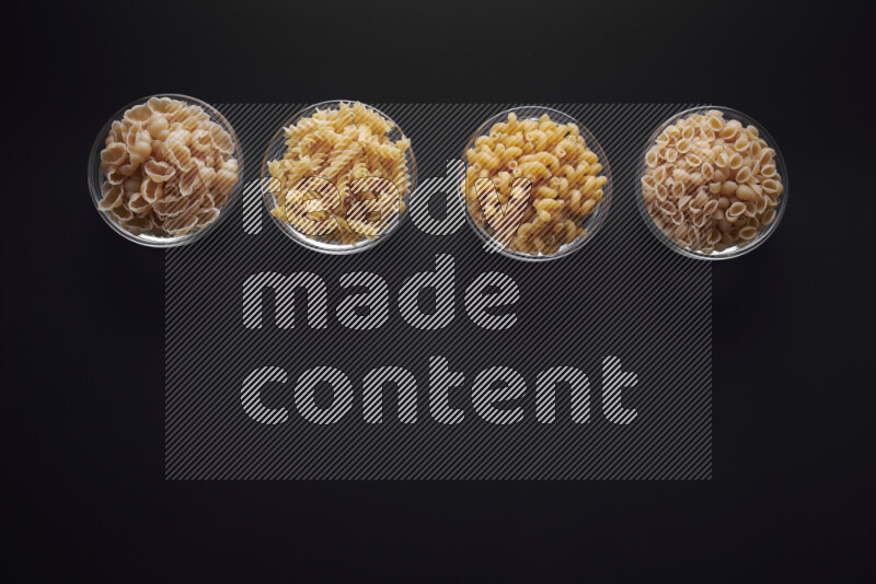 Different pasta types in glass bowls on black background
