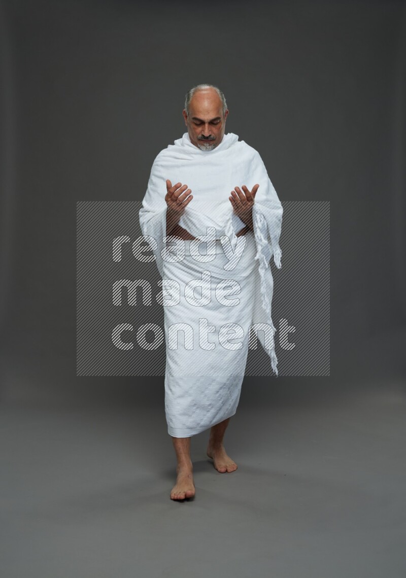 A man wearing Ehram Standing dua'a on gray background