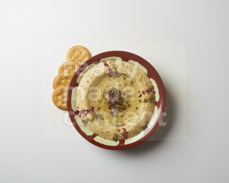 Hummus in a traditional plate garnished with zaatar & sumak on a white background