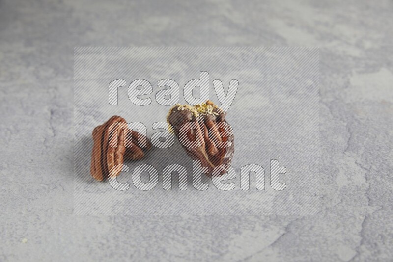pecan stuffed date covered with Dark chocolate and chopped pistachios on alight grey background