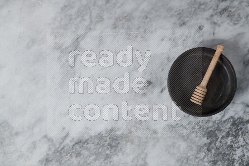 Black pottery oven plate with wooden honey dipper in it on grey marble background