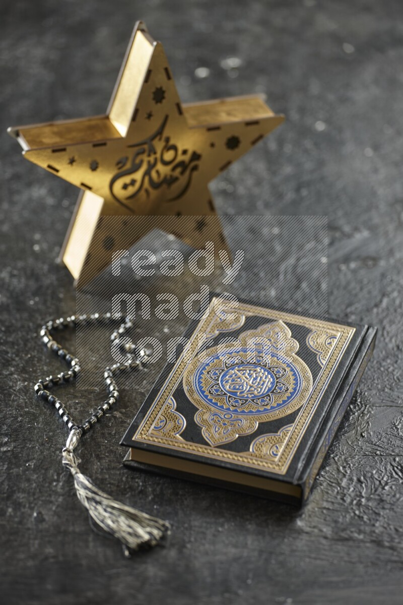 A wooden golden star lantern with different drinks, dates, nuts, prayer beads and quran on textured black background