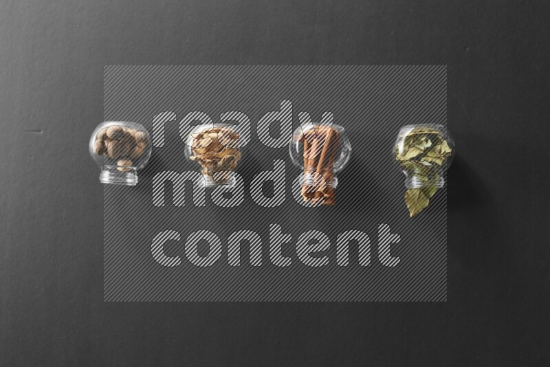 4 glass spice jars full of laurel bay leaves, ginger, cinnamon and nutmeg on black flooring