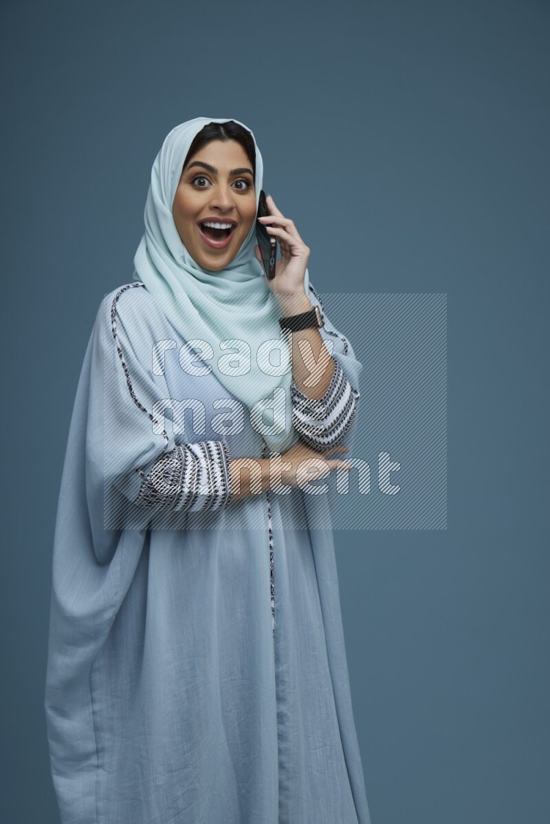 A Saudi woman having a Call in a blue background wearing blue Abaya with hijab