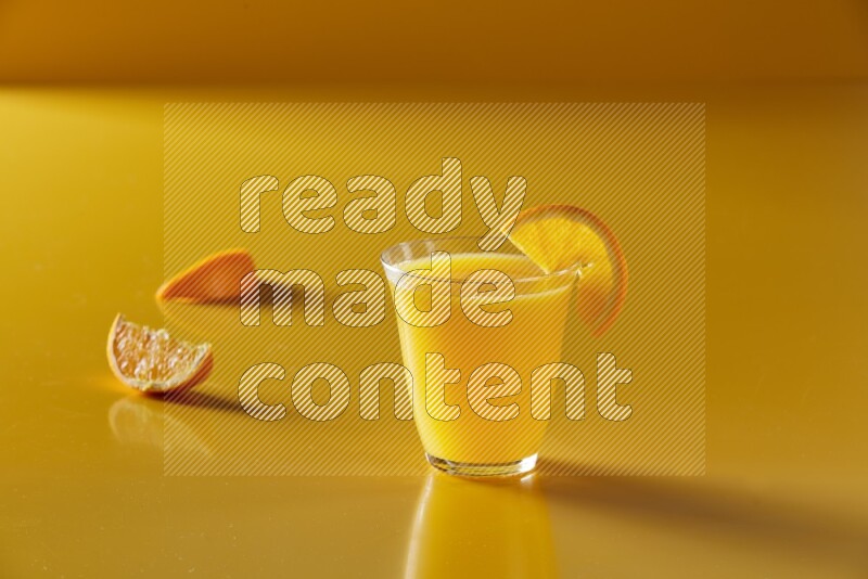 glass of orange juice with orange slice on yellow background