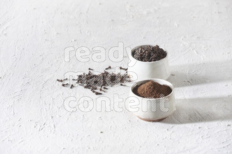 2 Beige ceramic bowls, one full of cloves and the other full of powder on textured white flooring