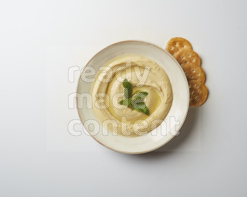 Hummus in a pottry plate garnished with mint  on a white background