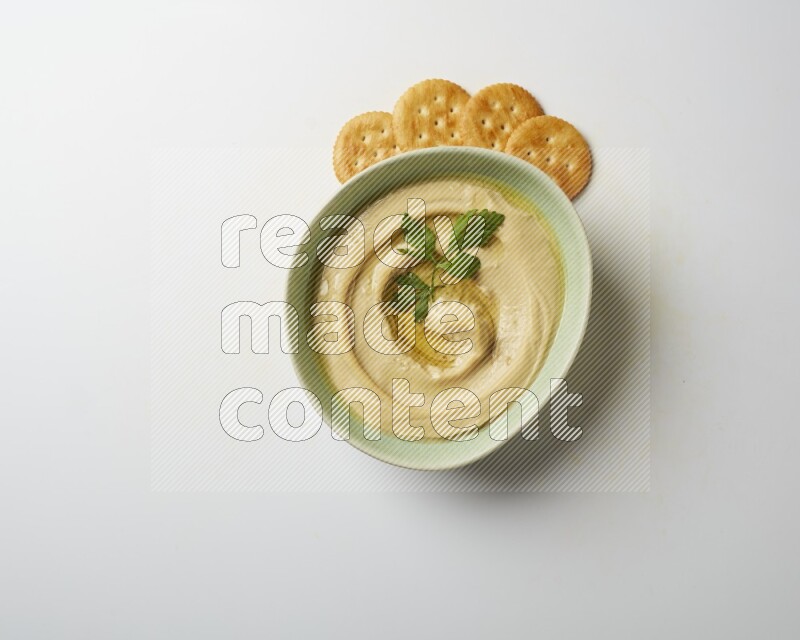 Hummus in a green plate garnished with parsley on a white background