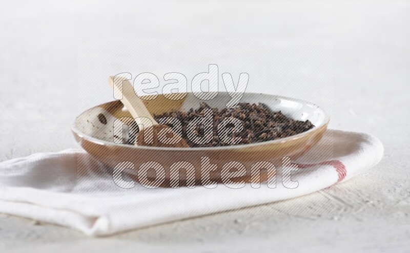 A Pottery plate full of whole cloves and a wooden spoon full of cloves powder in it on a textured white background
