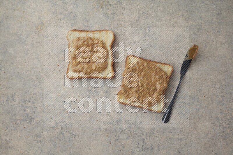 Crunchy  peanut butter on a toasted white toast slices with a spreading knife on a light blue textured background
