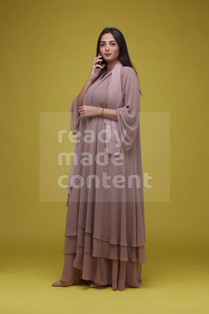 A woman Calling on a Yellow Background wearing Brown Abaya