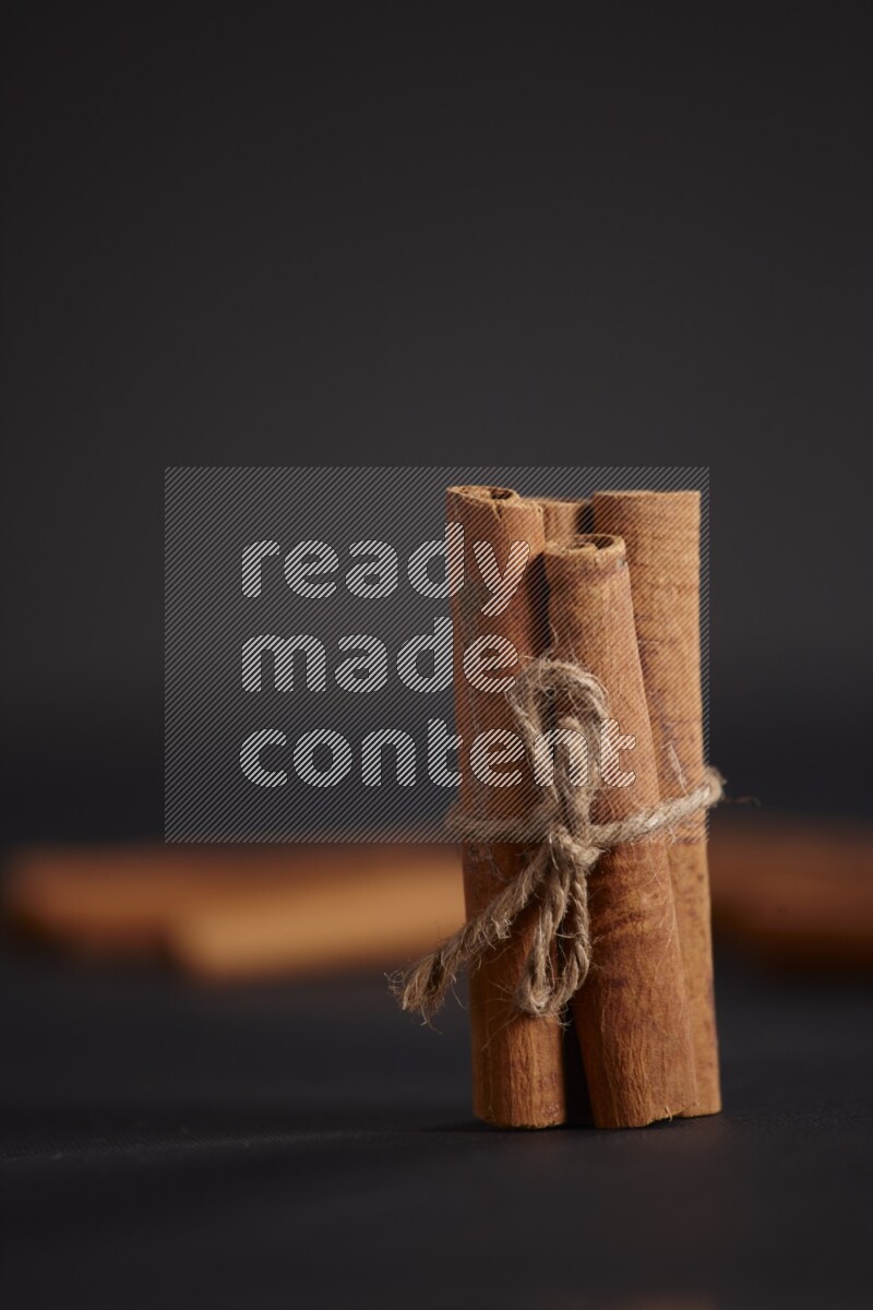 4 Cinnamon sticks stacked and bounded with more sticks in the background on black flooring