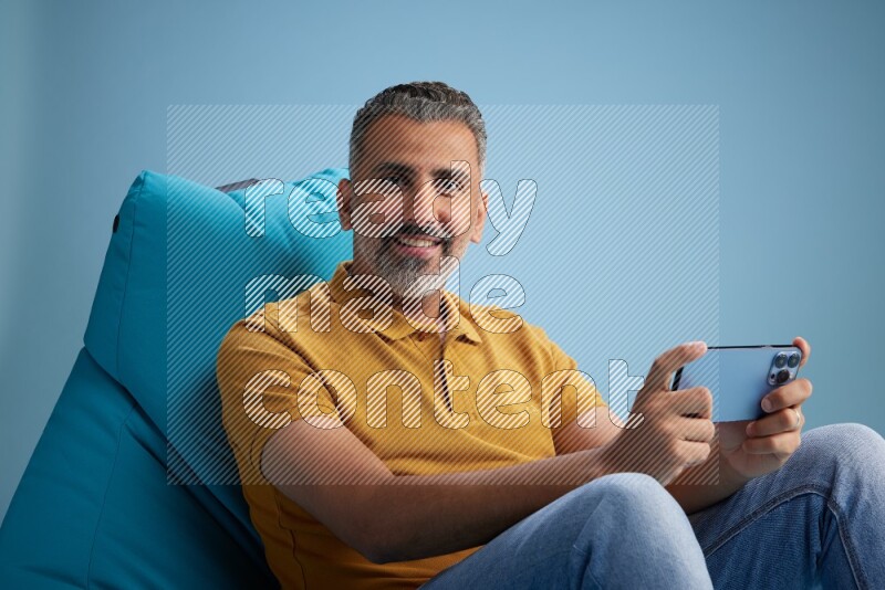 A man sitting on a blue beanbag and playing on phone