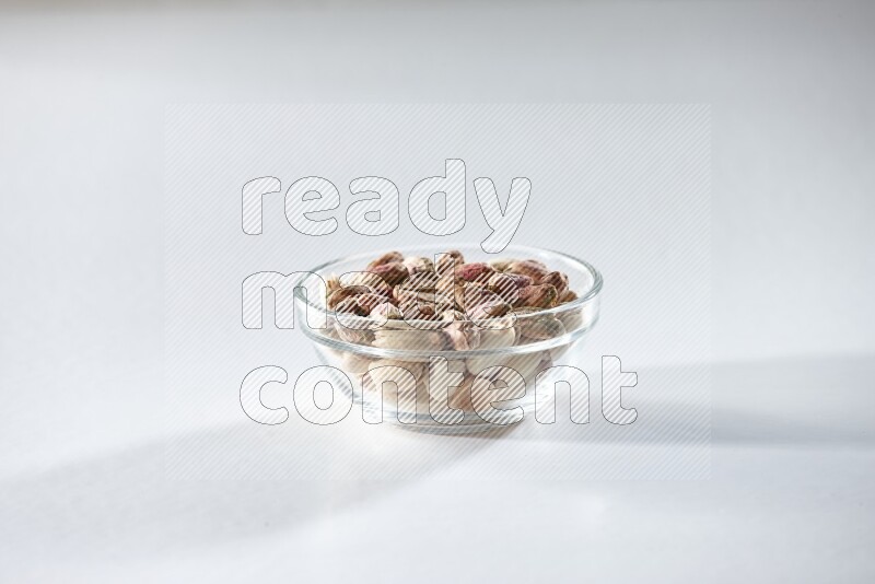 A glass bowl full of peeled pistachios on a white background in different angles