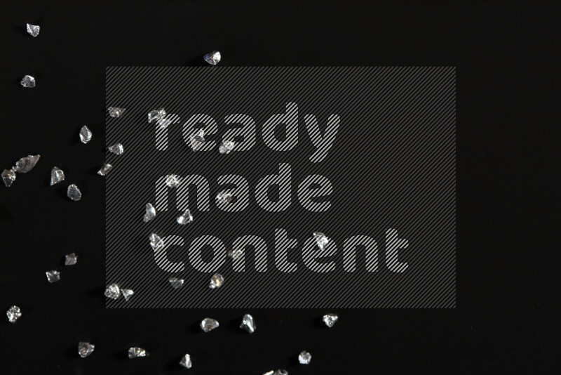 Silver shimmering fragments of glass scattered on a black background