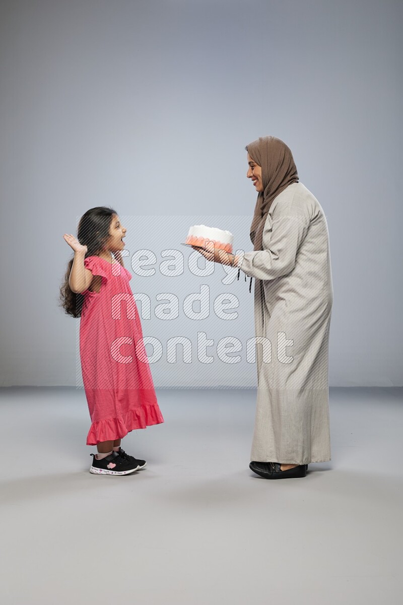 A mother giving a cake to her daughter on gray background