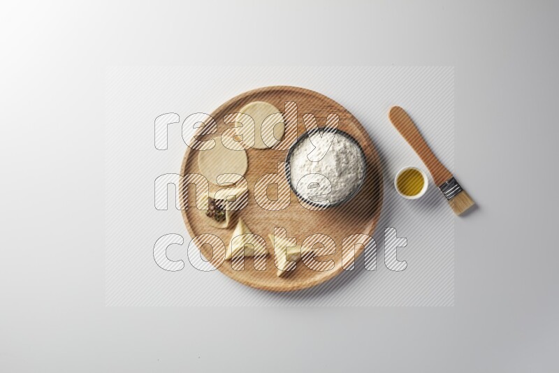 two closed sambosas and one open sambosa filled with meat while flour, and oil with oil brush aside in a wooden dish on a white background