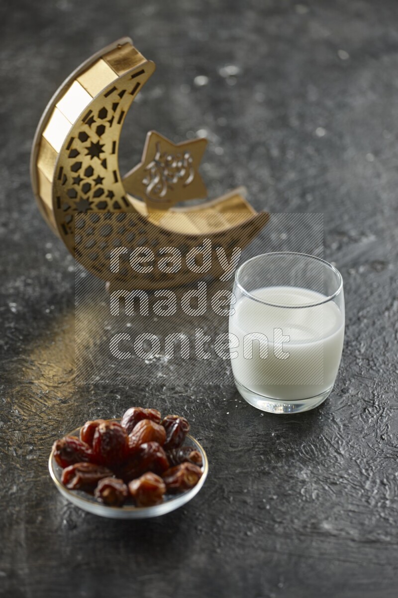 A wooden golden crescent lantern with different drinks, dates, nuts, prayer beads and quran on textured black background